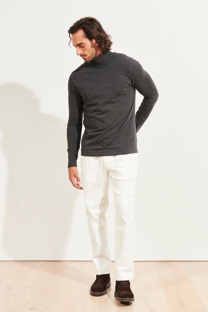 Homme portant un col roulé en coton pima gris avec un pantalon blanc, dans un environnement minimaliste.