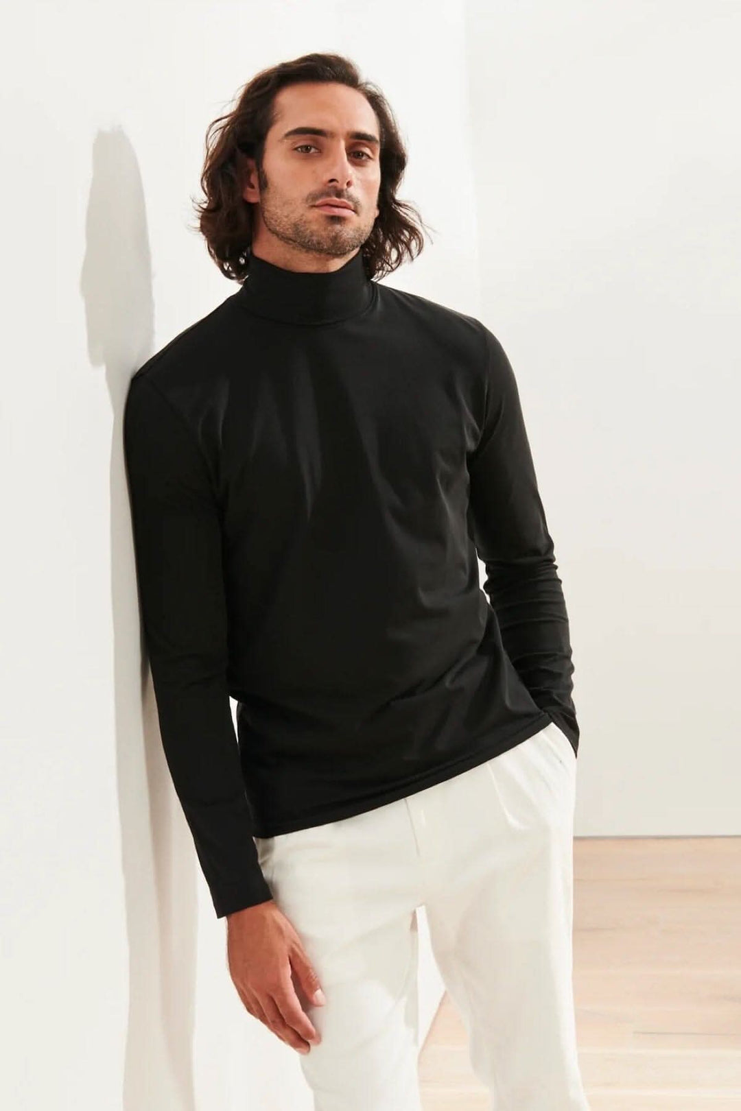 Homme portant un col roulé en coton pima noir, élégamment stylé avec un pantalon blanc.