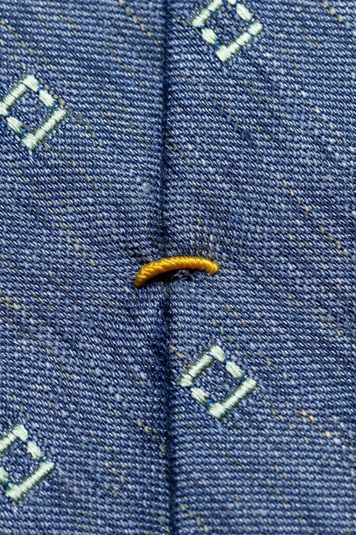 Détail d'une cravate à motifs, mettant en valeur un point de couture avec un fil jaune sur un tissu en soie.