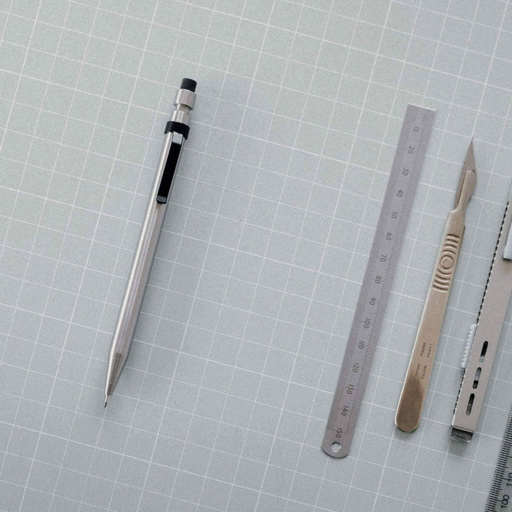Crayon Modern Fuel en métal solide avec règle et outils sur fond de papier quadrillé.