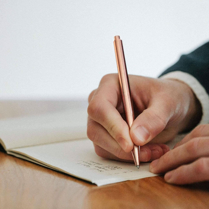 Main image of a person writing with a metallic Crayon Modern Fuel pencil on a notepad.