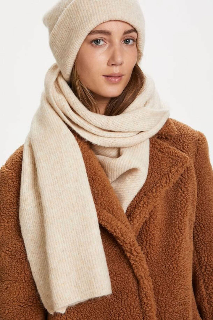 Foulard Solla en beige, classique et élégant, porté avec un manteau en fausse fourrure et un bonnet, parfait pour l&