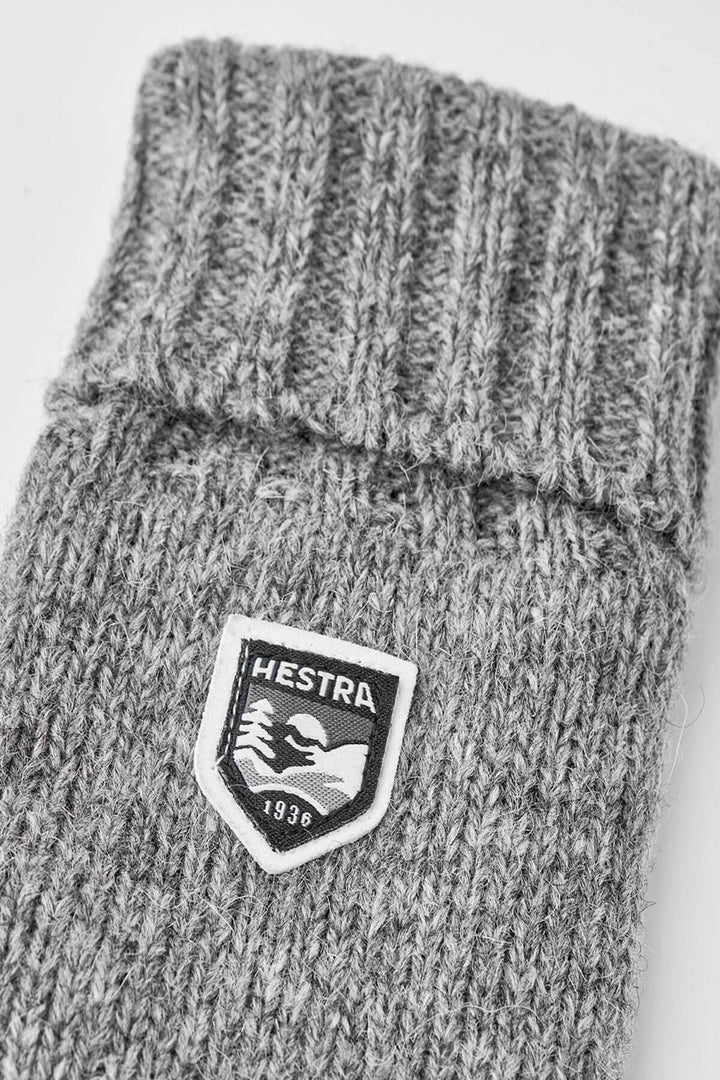 Gant en laine gris avec logo Hestra, texture tricotée et finition côtelée, parfait pour l'hiver.