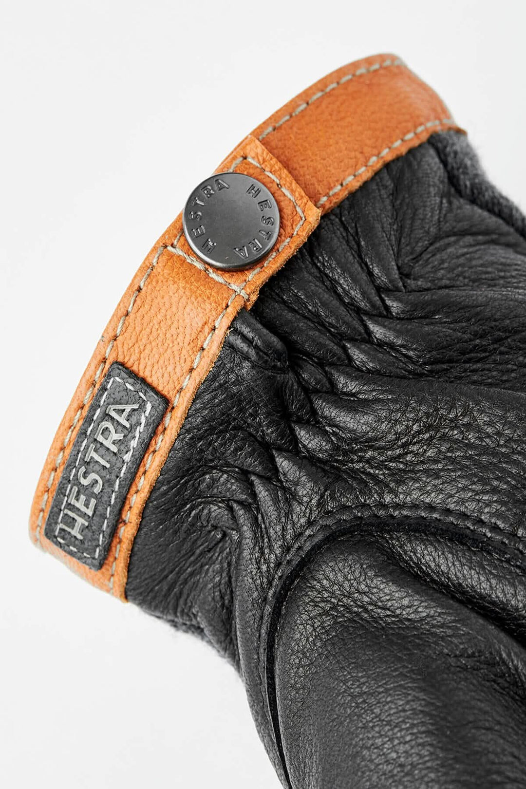 Gant en cuir noir avec une manchette en cuir orange et un logo Hestra sur le poignet.