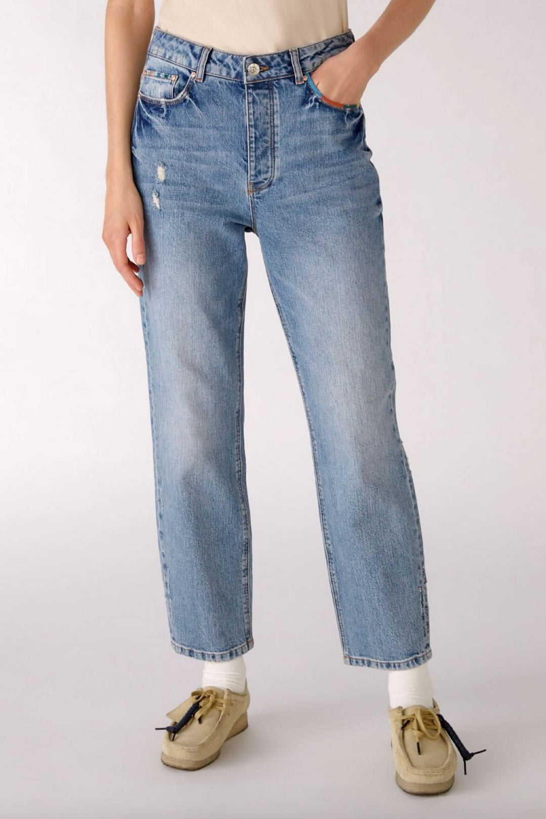 Jean pâle à jambe droite avec détails de coutures colorés, porté avec un haut basique.