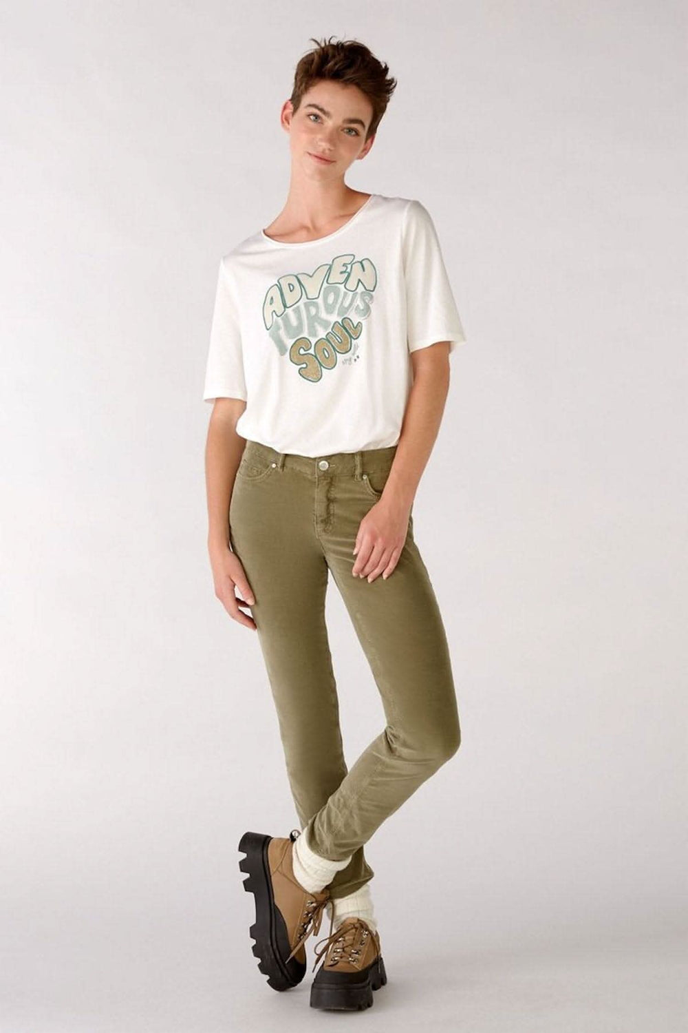 Femme portant des jeans en velours verts avec un t-shirt blanc, style décontracté, prêt pour l'aventure.