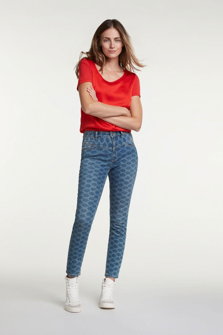 Femme portant des jeans imprimés motif "bizous" avec un haut rouge, style élégant et confortable.