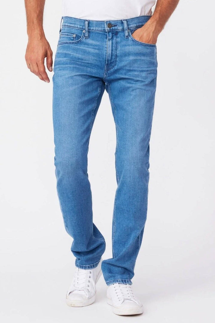 Jeans Paige Lennox Boxter en délavage moyen, coupe ajustée, portés par un homme avec des chaussures blanches.