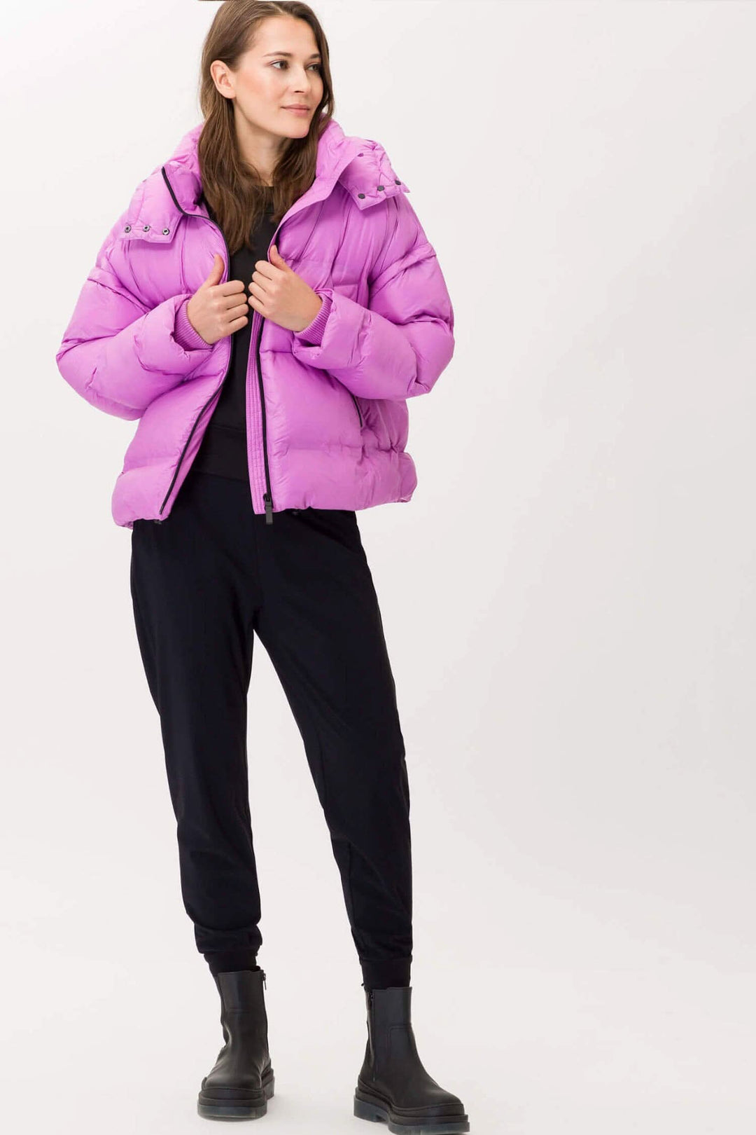 Femme portant un manteau capitonné rose avec capuchon, stylé et tendance, associé à un ensemble noir.