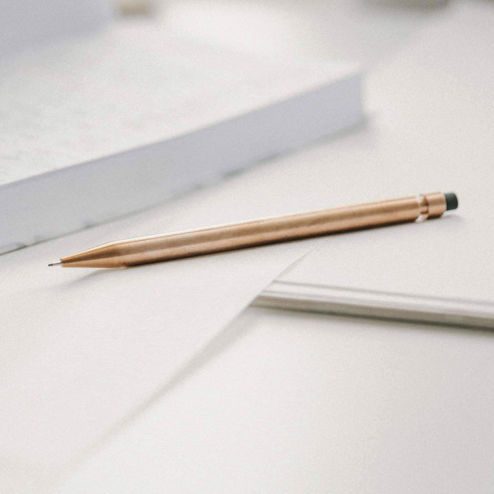 Crayon Modern Fuel en métal, élégant et sans plastique, posé sur une feuille de papier, avec un bloc-notes en arrière-plan.