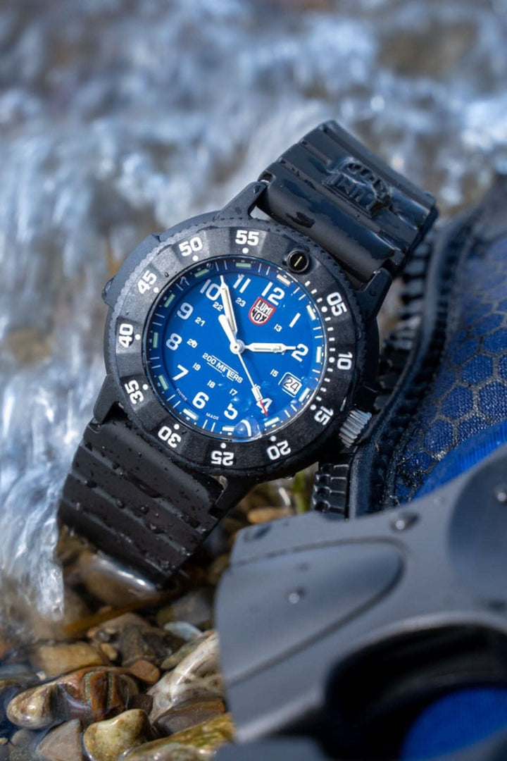 Montre Luminox Navy SEAL 3003.EVO, étanche, cadran bleu, bracelet noir, sur fond de rochers et eau.