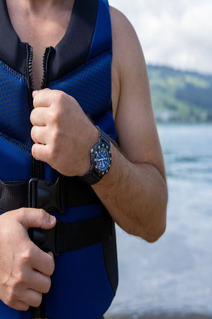 Homme en gilet de sauvetage montrant une montre Luminox Navy SEAL au bord de l'eau.