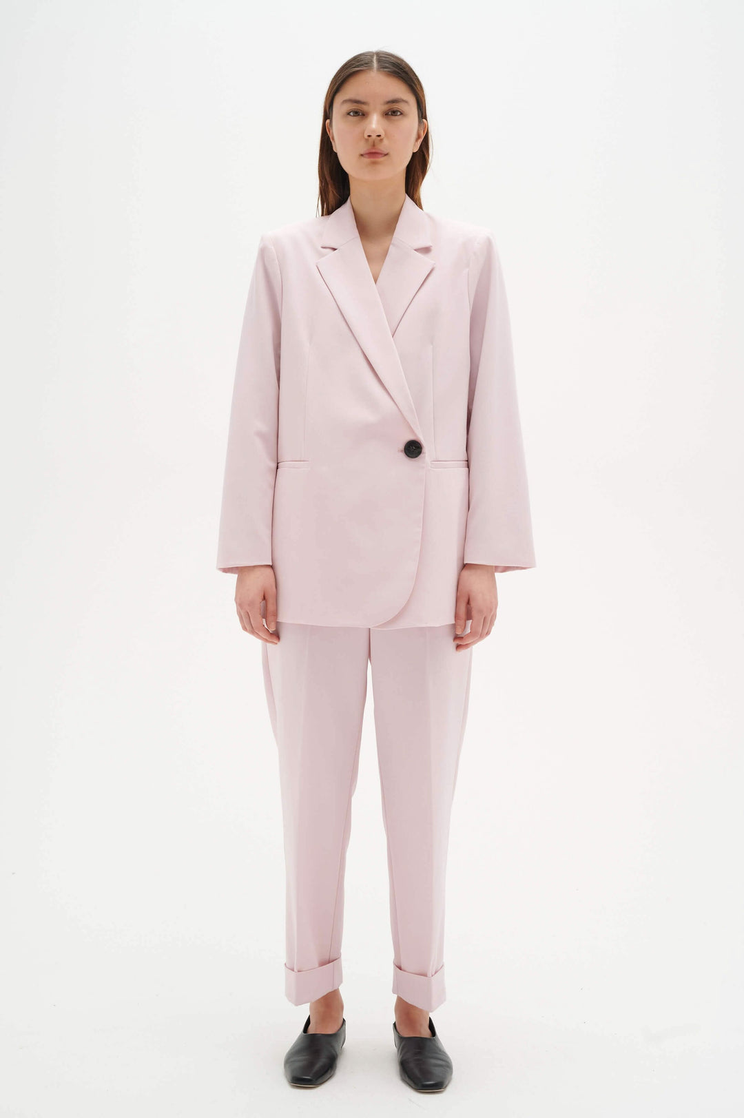 Femme portant un tailleur rose clair avec un pantalon à revers et une veste à bouton pour un look élégant.