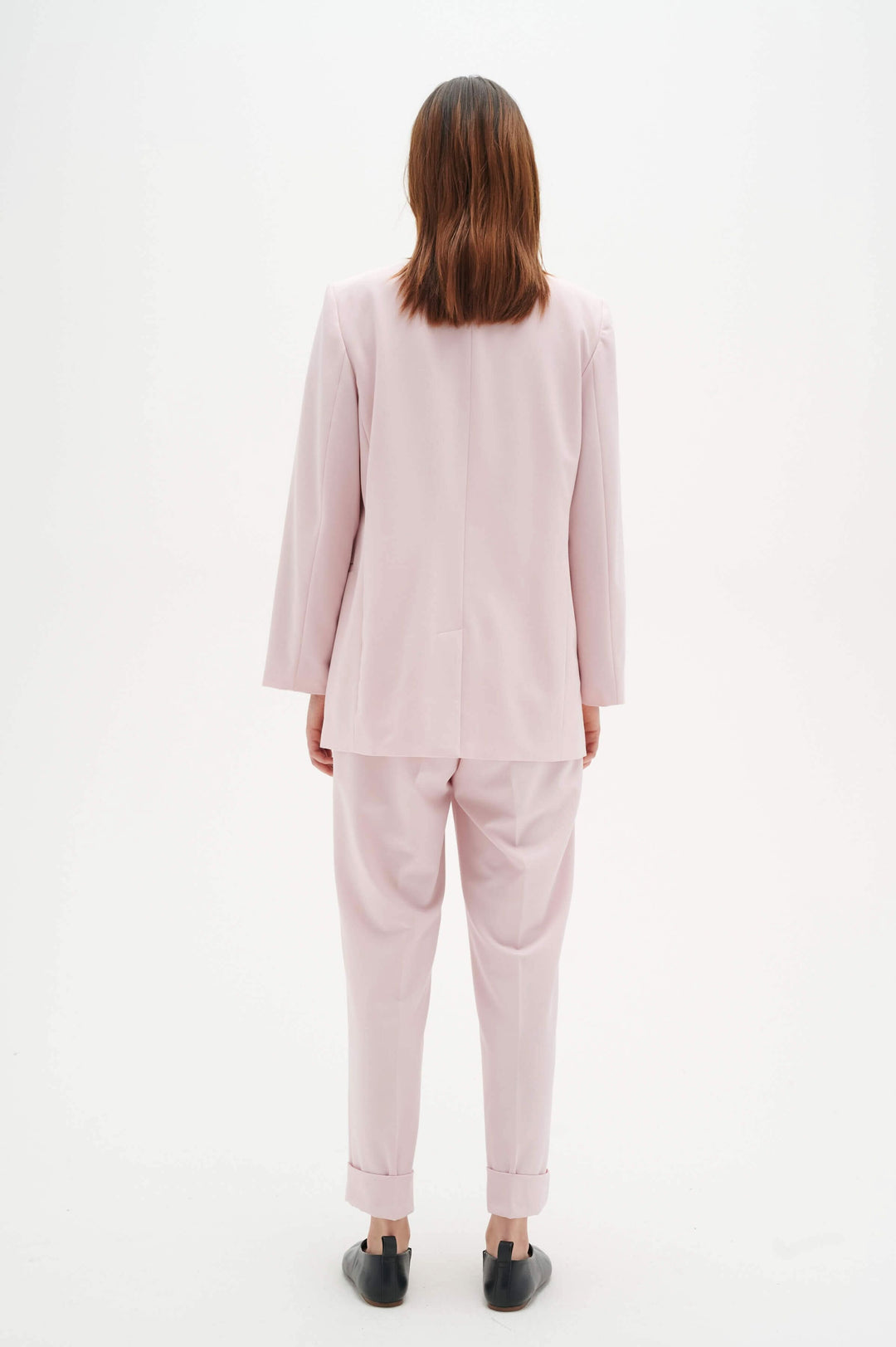 Femme vue de dos portant un ensemble en rose, avec blazer et pantalon à revers élégant.
