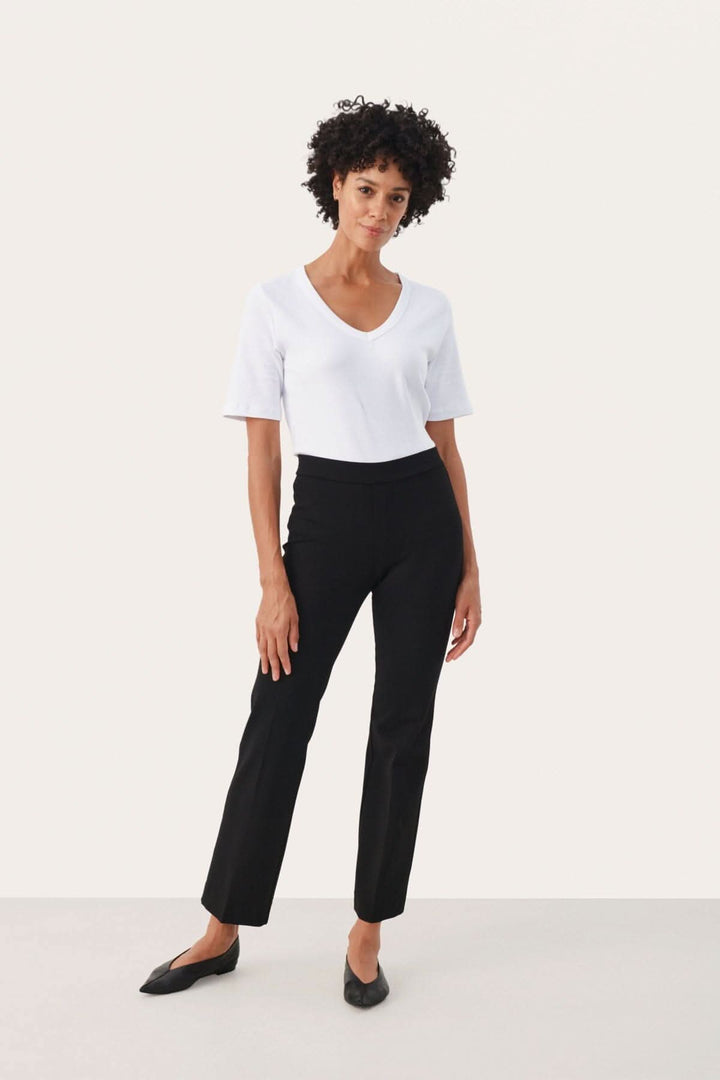 Femme portant un pantalon classique Ponta noir et un T-shirt blanc dans un décor minimaliste.