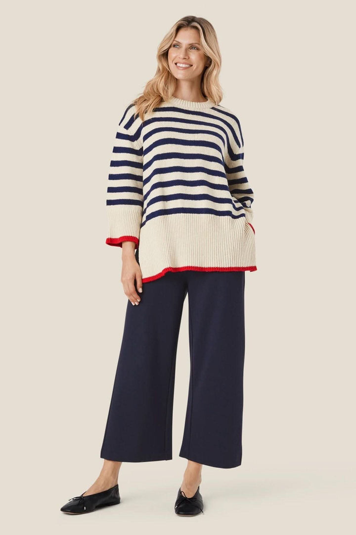 Femme portant un pull rayé beige et bleu avec un pantalon large bleu marine, style décontracté et confortable.