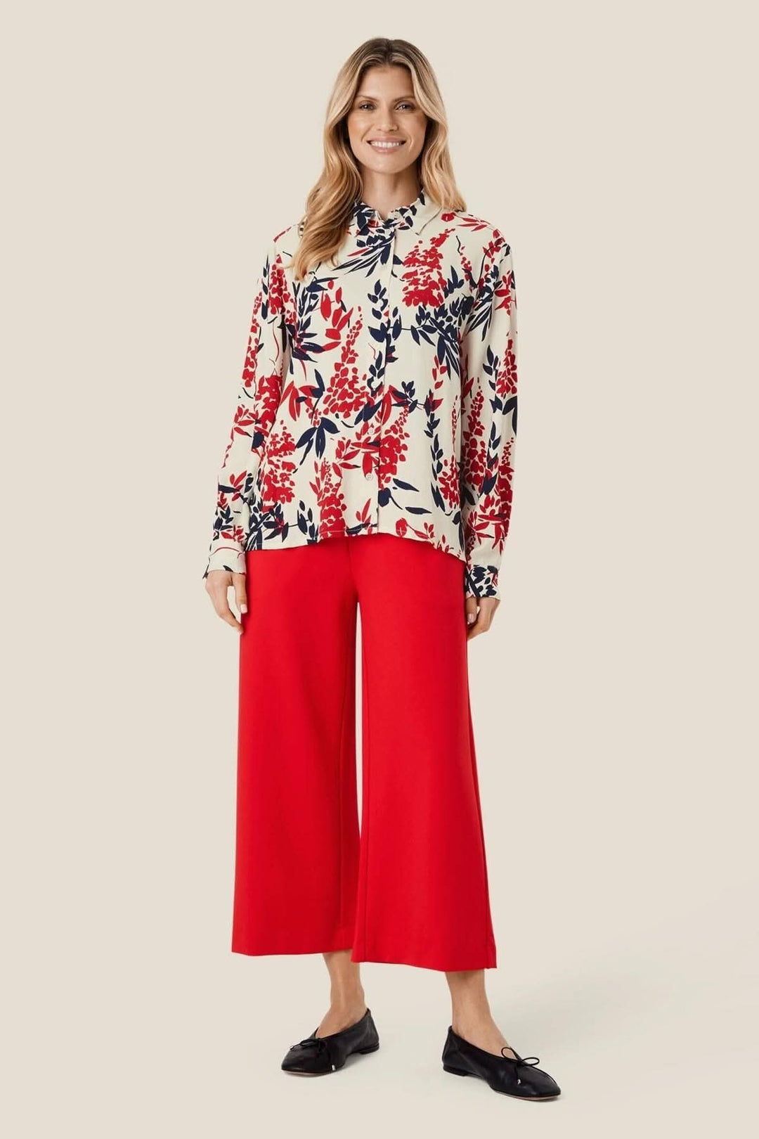 Femme portant un pantalon en jersey rouge et un haut à motif floral, affichant un style décontracté et élégant.
