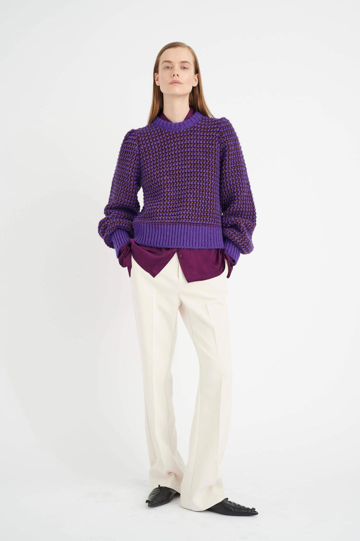 Modèle féminine portant un pull violet et un pantalon clair, présentant une tenue moderne et élégante.