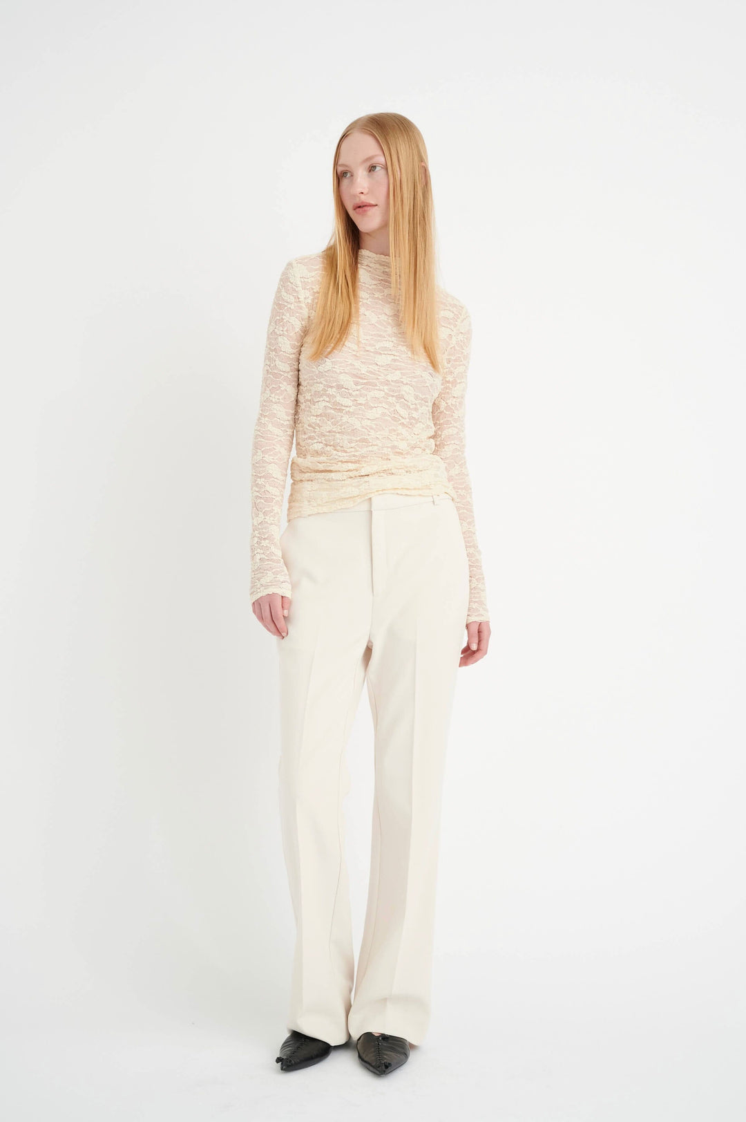Modèle portant un pantalon Ibbie habillé, jambe droite, couleur crème, avec un haut à manches longues.