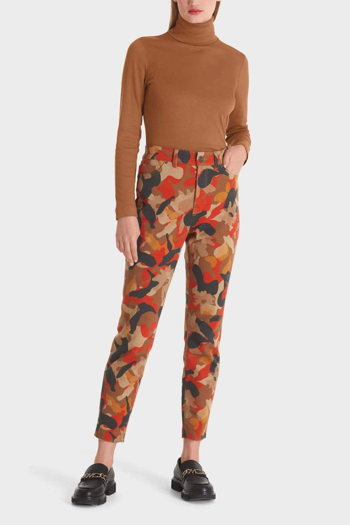 Pantalon camouflage coloré en coton bio à fermeture bouton et zip, porté avec un haut à col roulé marron.