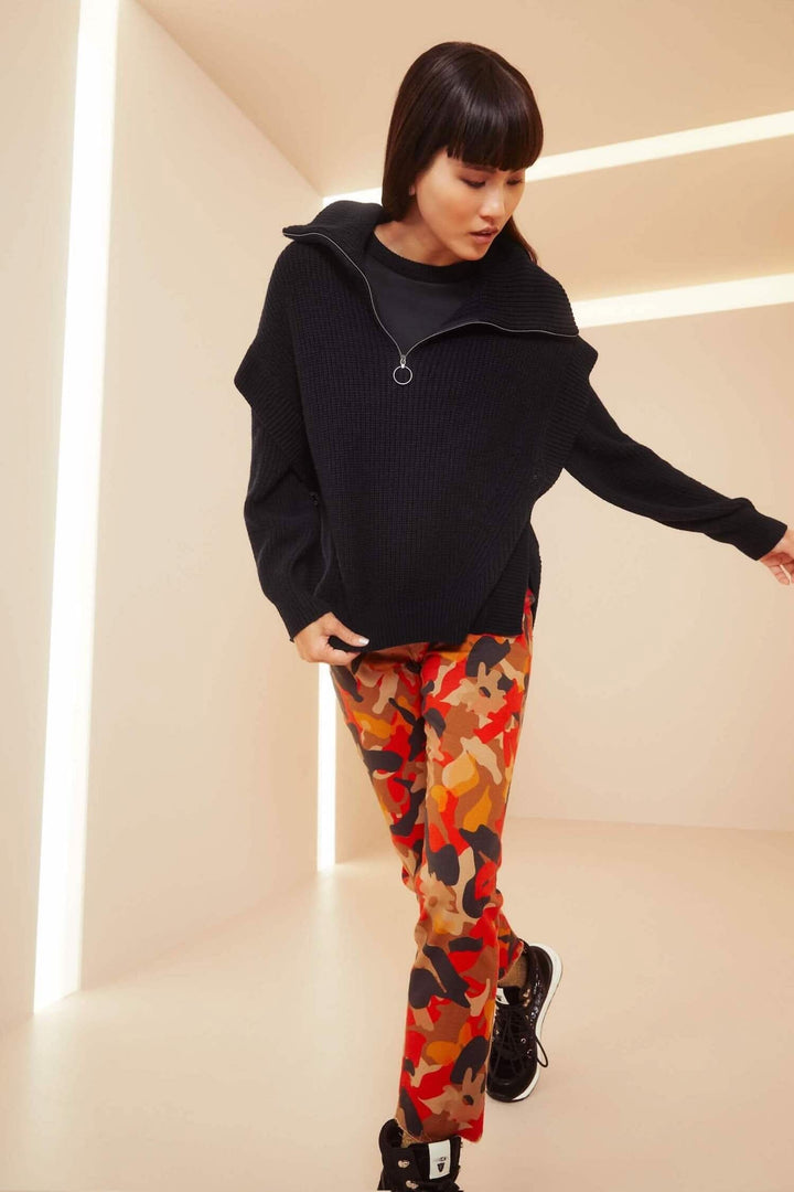Femme portant un pull noir et un pantalon imprimé camouflage coloré, style slim fit, dans un environnement contemporain.