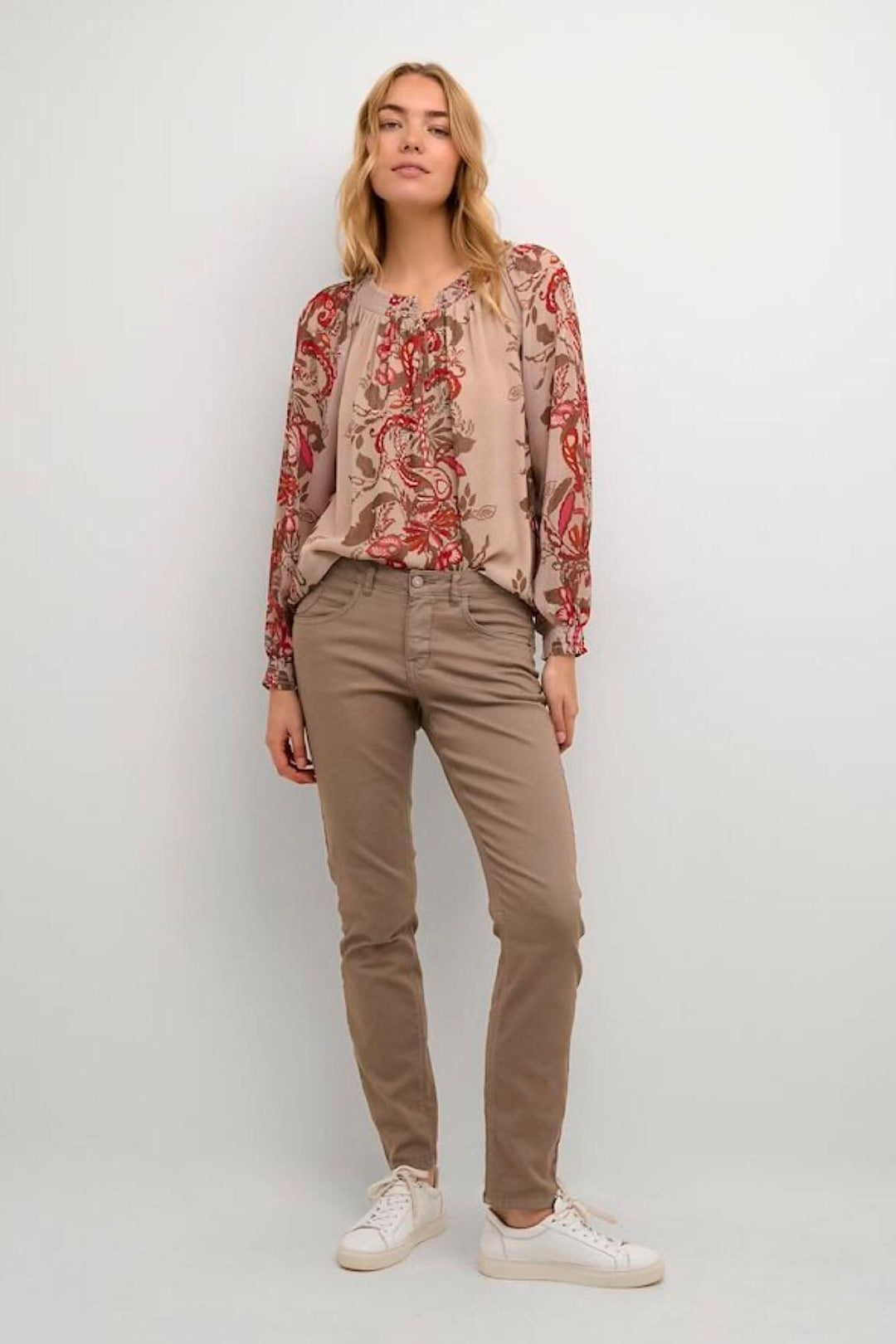 Femme portant un pantalon style jean étroit beige avec blouse à motifs floraux rouges.