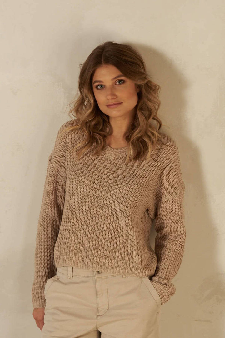 Pull à mailles en coton beige avec col en v, modèle à manches et couture légèrement tombante.