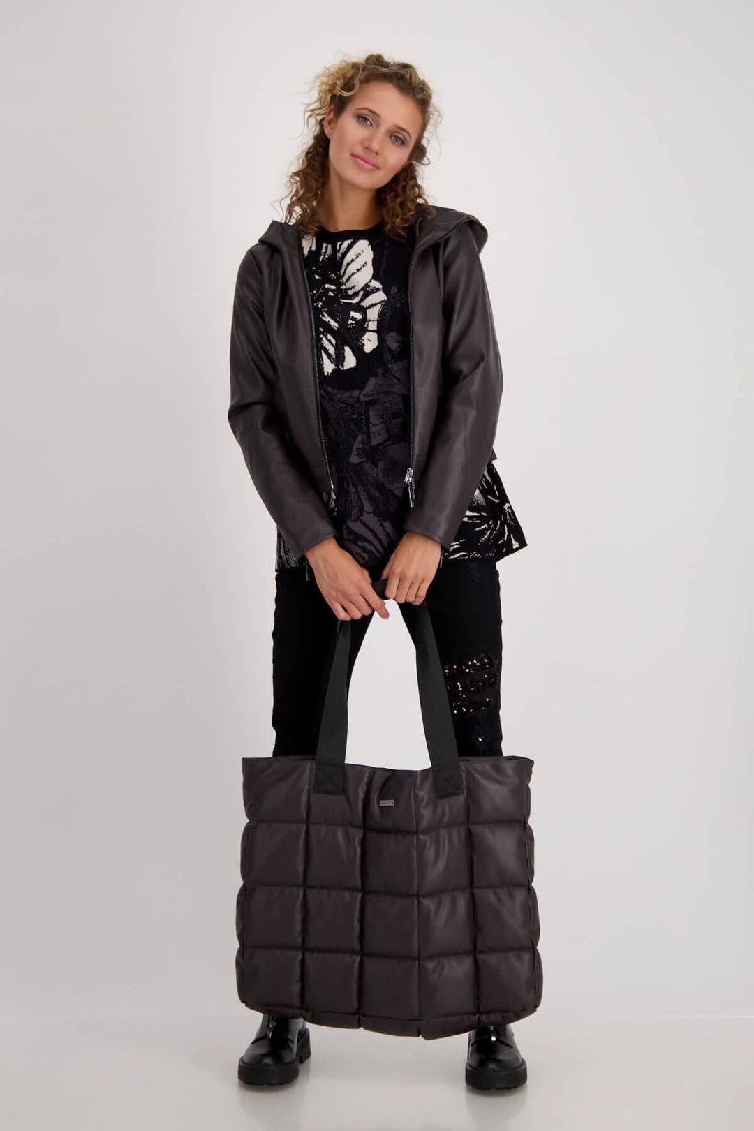 Femme portant un sac cabas matelassé noir avec une veste et un haut à motifs floraux.