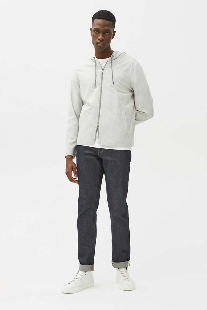 Homme portant une chemise en tissu technique légère avec capuche, jeans foncés et baskets blanches.