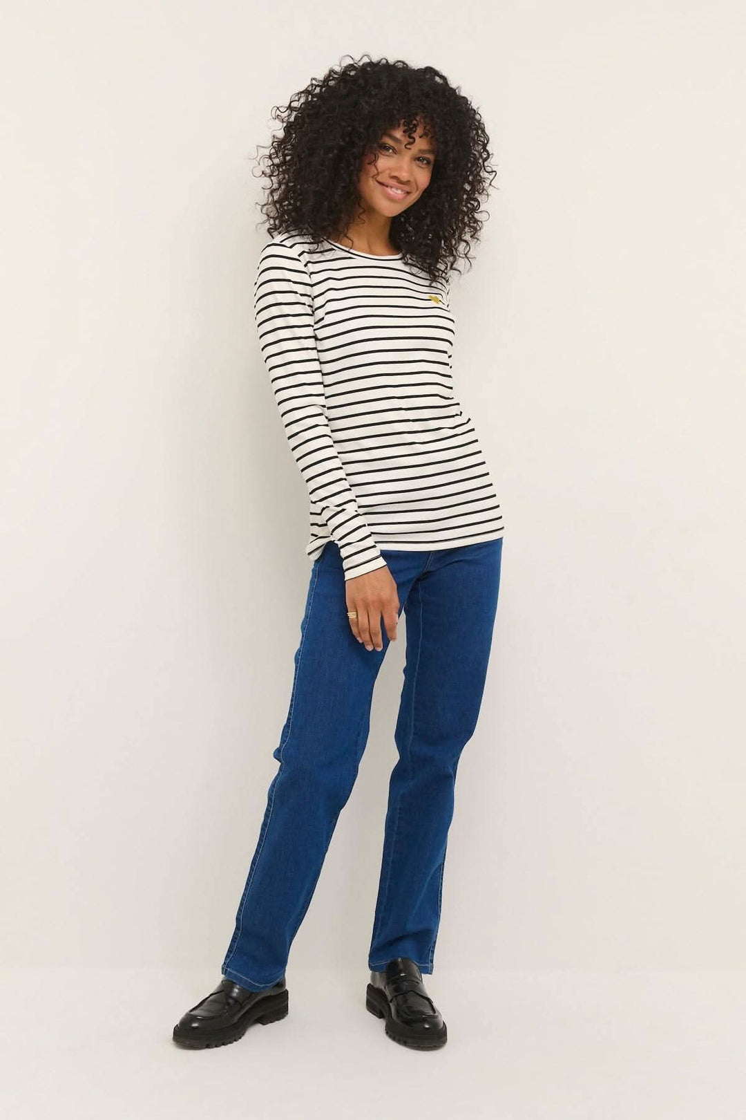 Femme souriante portant un t-shirt rayé à manches longues Lidy avec un cœur cousu, associé à un jean bleu.