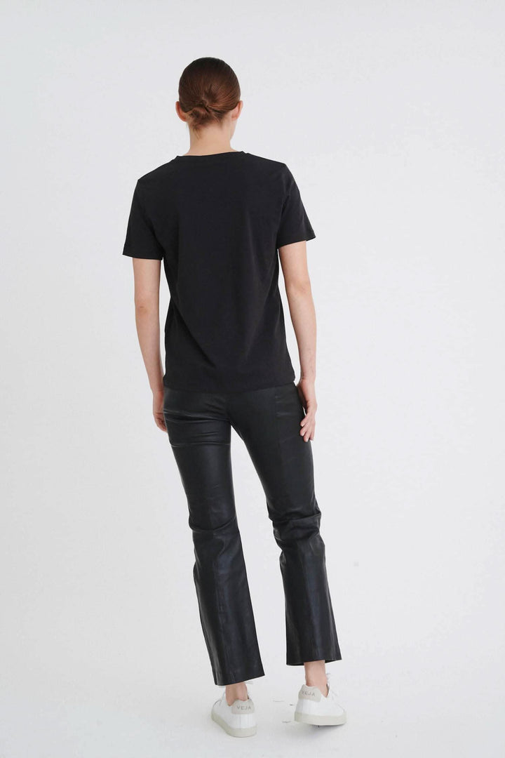 Femme portant un t-shirt noir col en V, vu de dos, avec un pantalon en cuir noir.