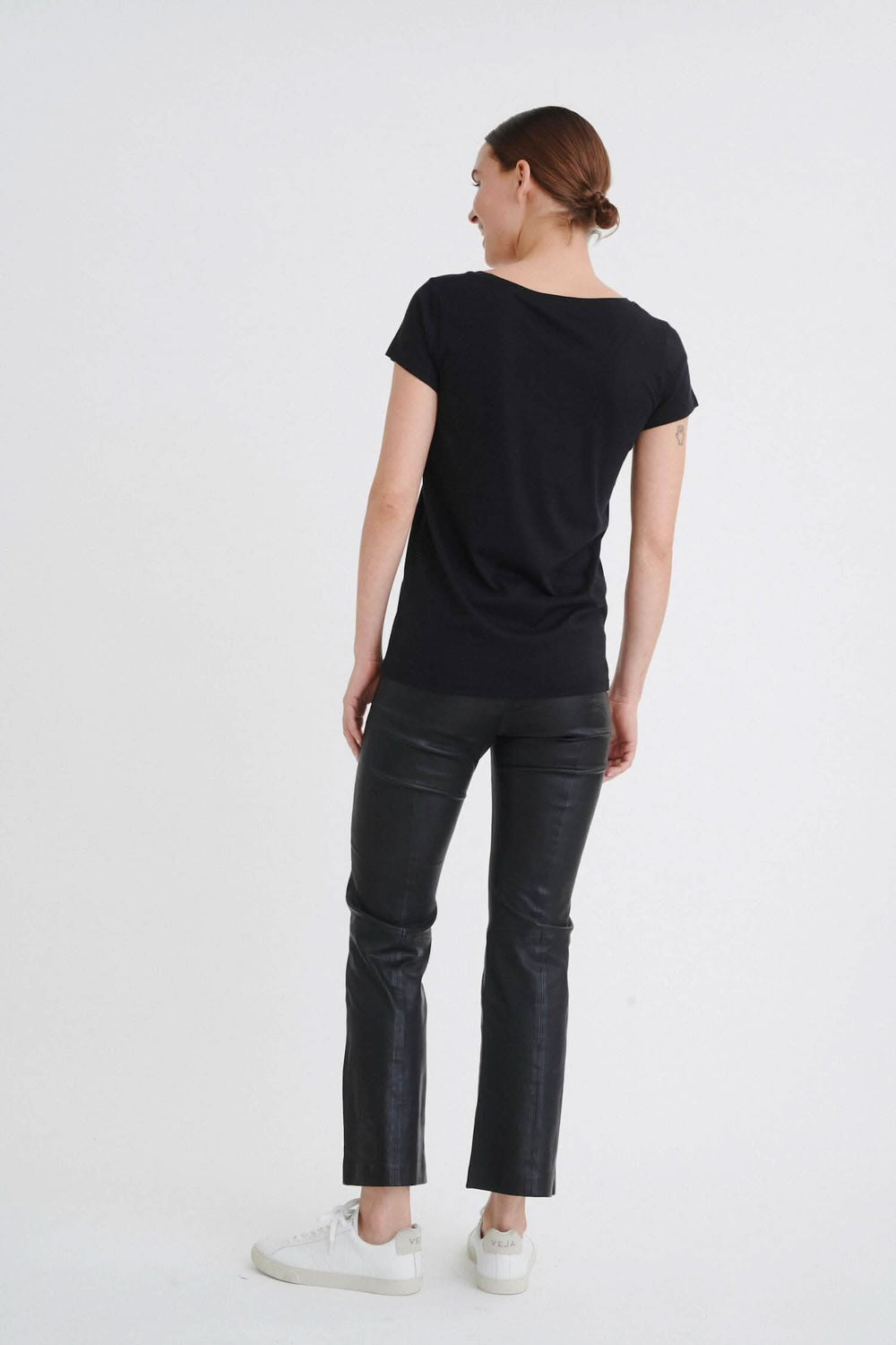 Femme portant un t-shirt noir à col rond et un pantalon en cuir, vue de dos.