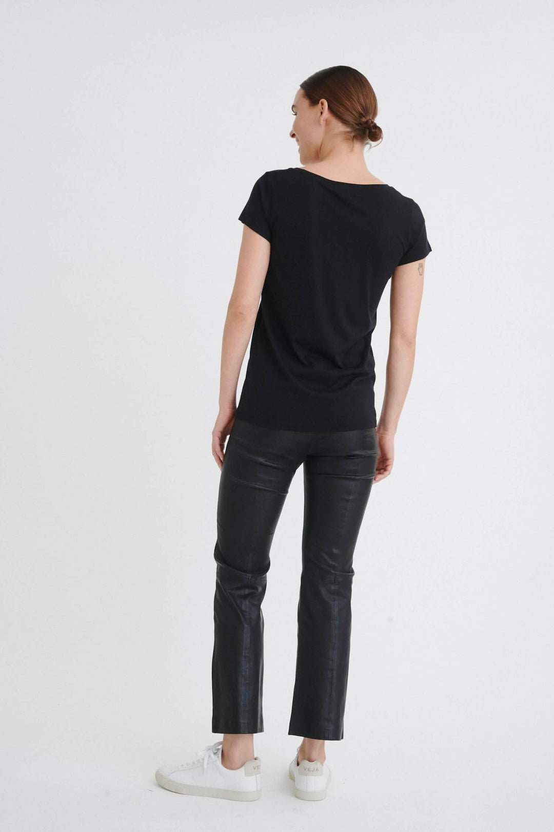 Femme portant un t-shirt noir à col rond et un pantalon en cuir, vue de dos.