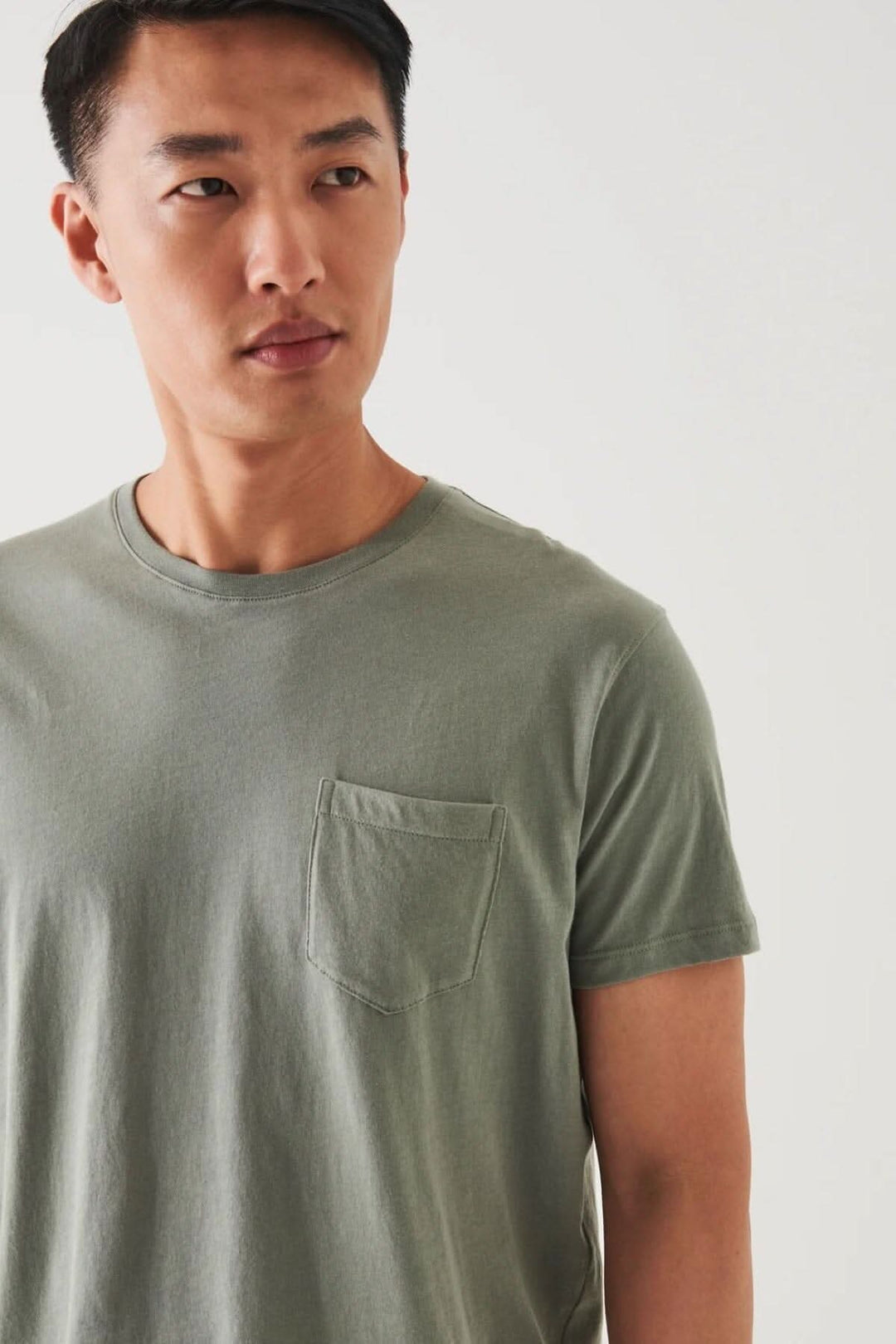 Homme portant un t-shirt léger en coton pima avec une poche, couleur olive, ajustement régulier, parfait pour temps chaud.