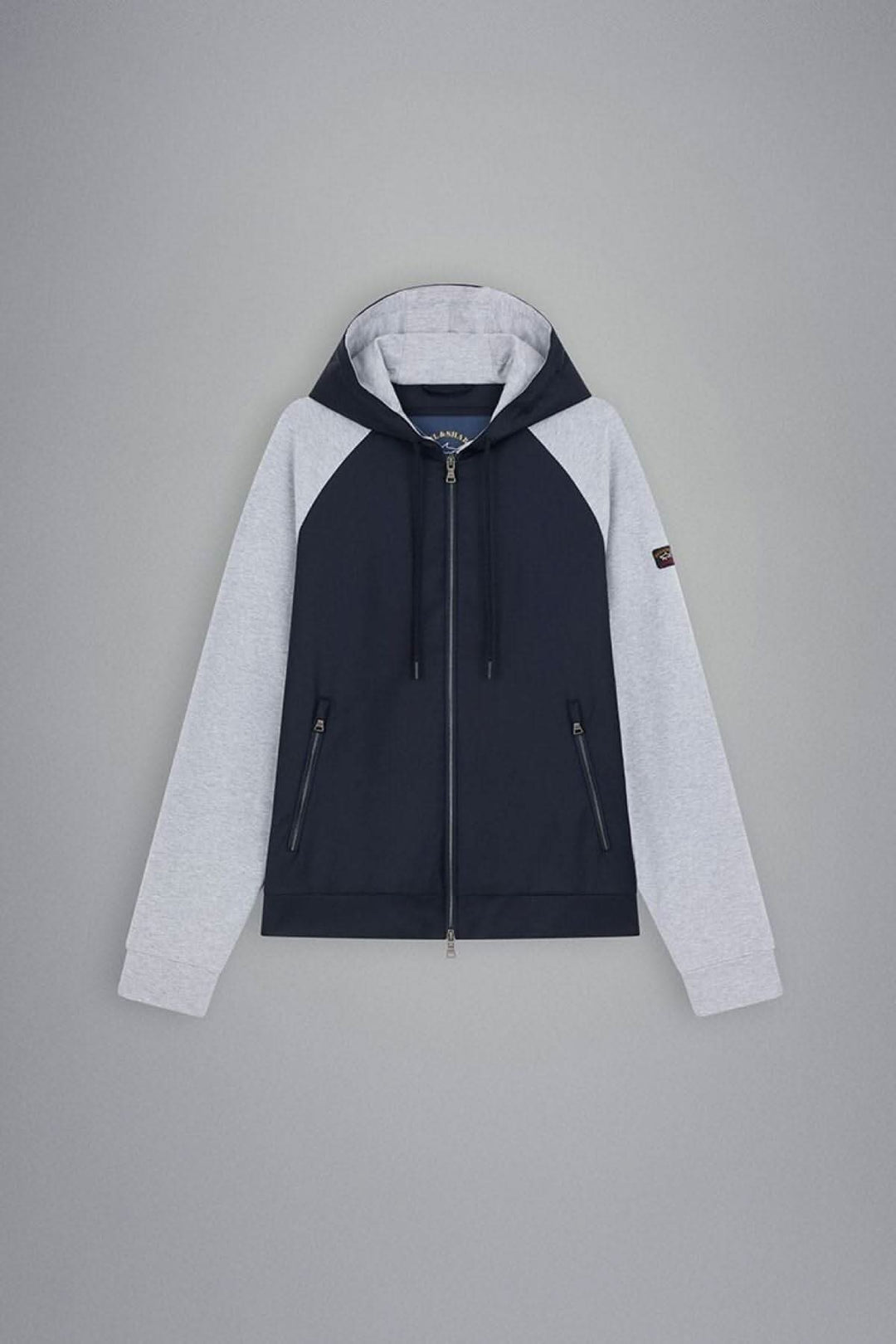 Veste à capuche à zip bleu marine et manches grises, avec logo sur la manche et poches zippées.