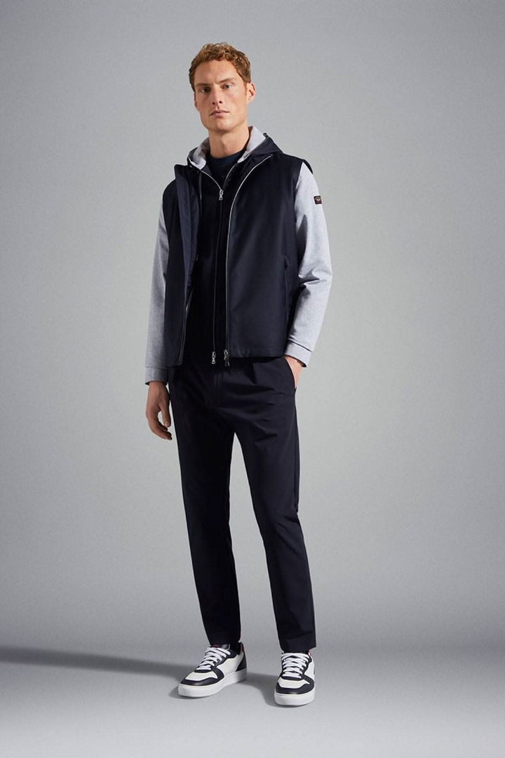 Homme portant une veste à capuche bleu marine avec logo, pantalon noir, et sneakers blanches.