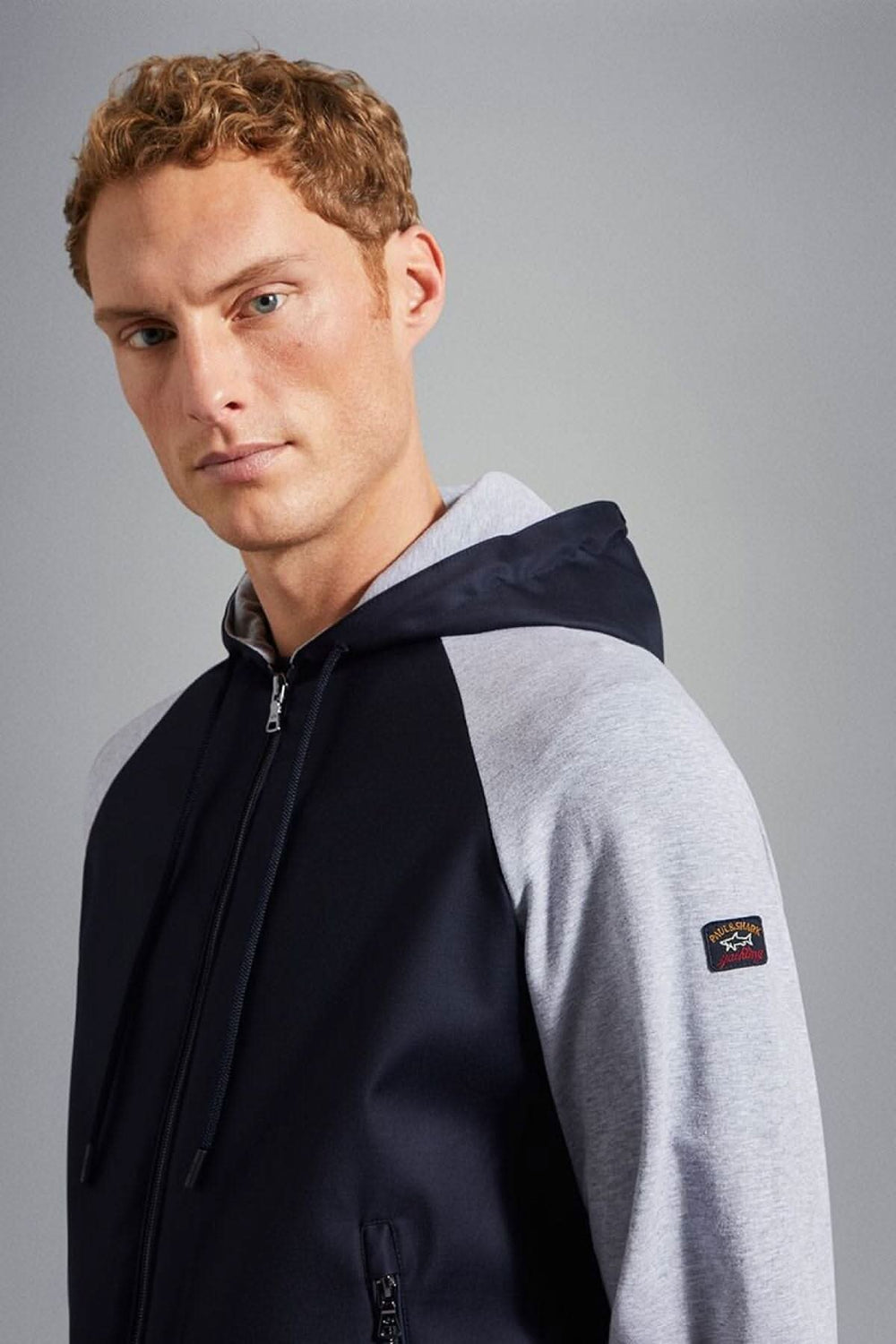 Homme portant une veste à capuche bleu marine avec logo sur la manche, face au caméraman.