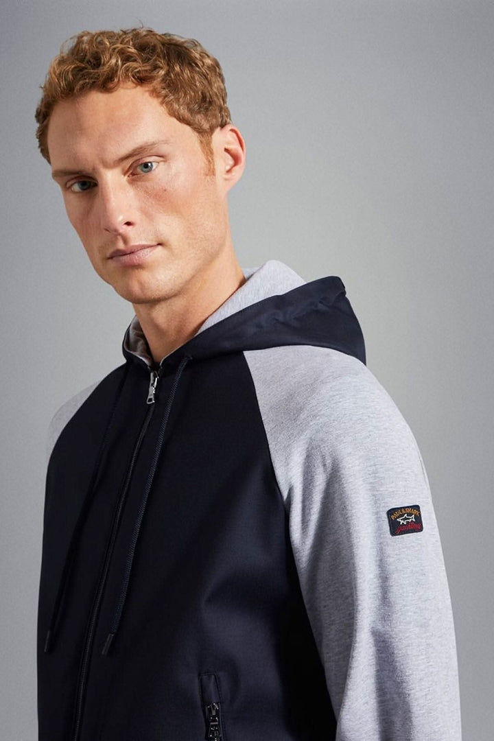 Homme portant une veste à capuche bleu marine avec logo sur la manche, face au caméraman.