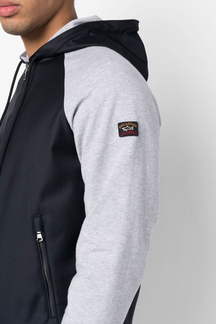 Veste à capuche bleu marine et gris avec logo sur manche, fermeture éclair et poches zippées.