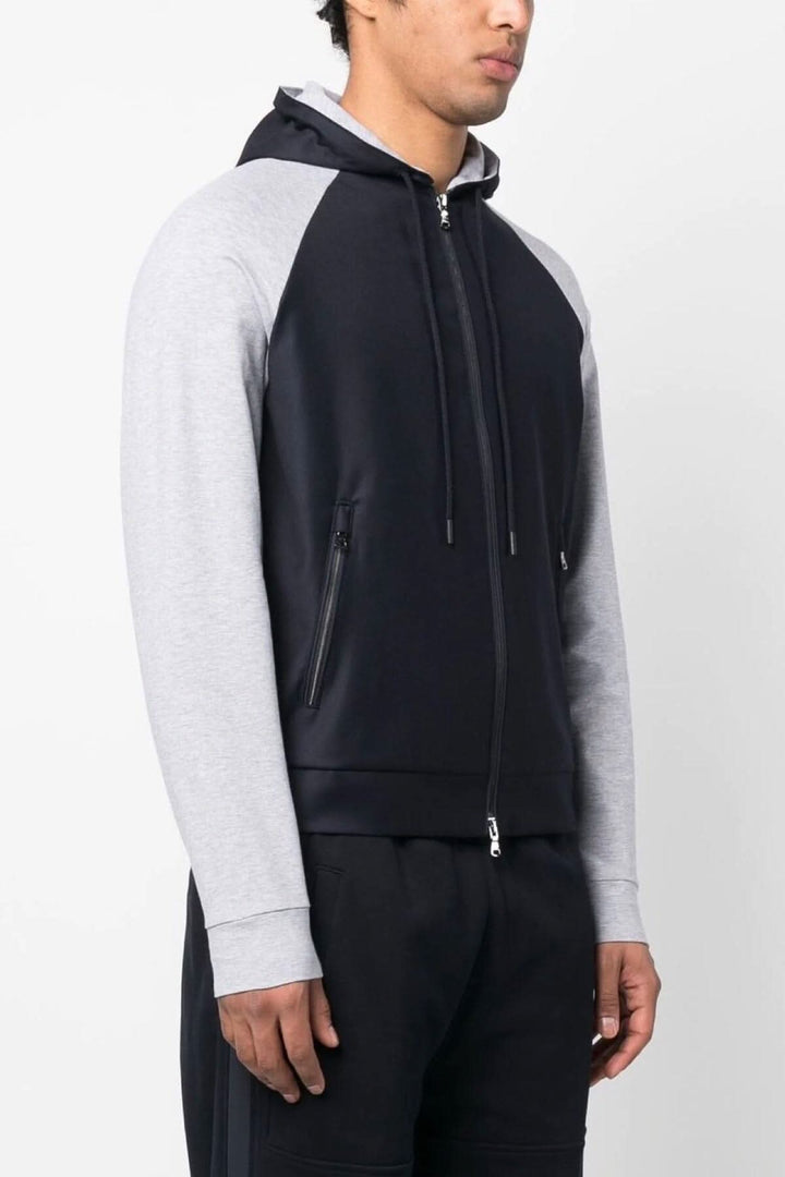 Veste à capuche noire avec manches grises, fermeture à glissière et logo, idéale pour le confort et le style.