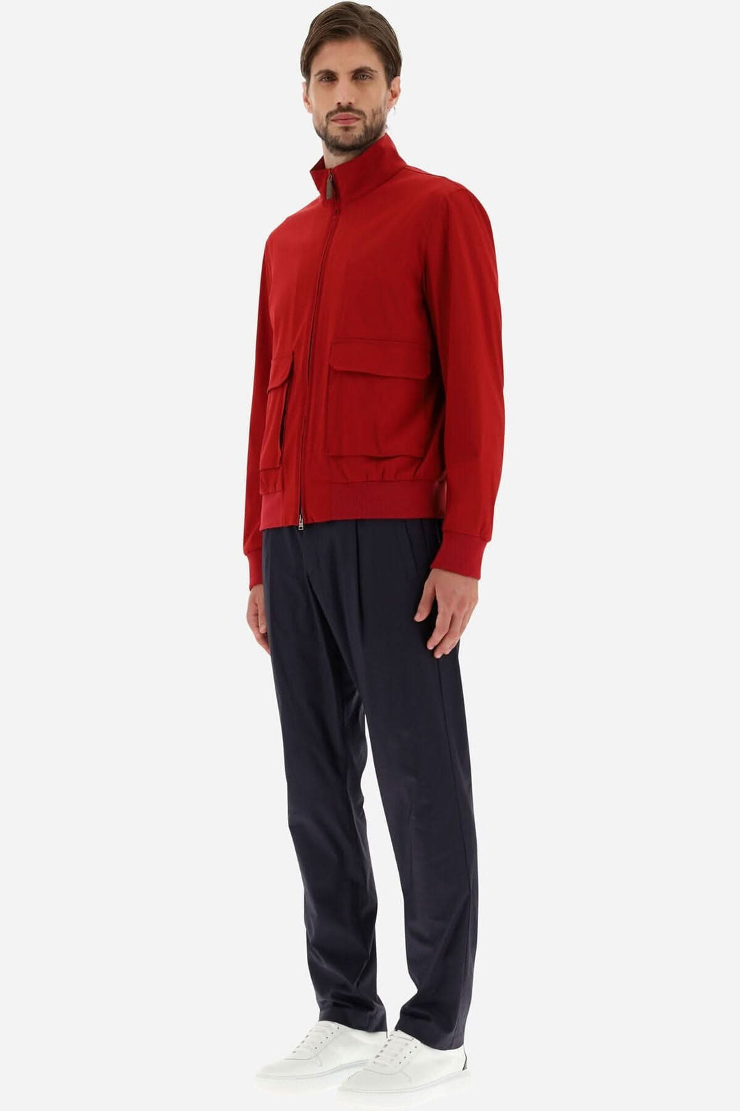Homme portant une veste bomber rouge en tissu T-Way, associée à un pantalon bleu marine et des chaussures blanches.